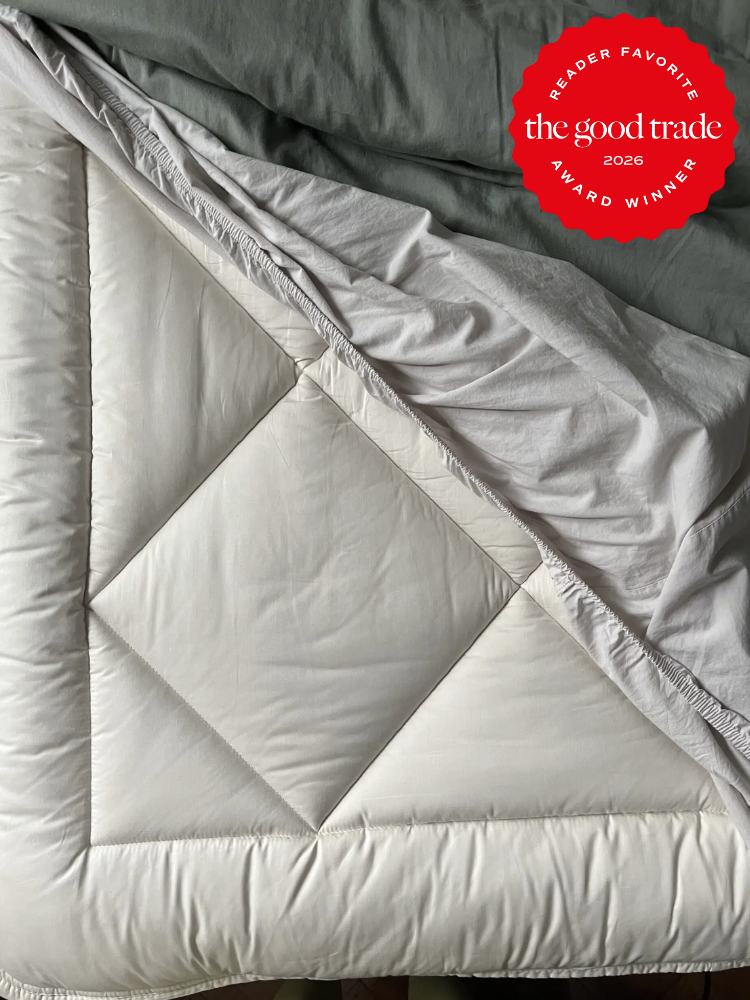 A close-up of a white comforter on a bed with a "The Good Trade 2026 Award Winner" badge in the top right corner.