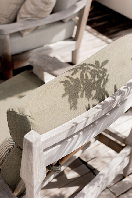 Close-up of a light green outdoor chair with a shadow of leaves cast on the backrest, positioned on a wooden deck.