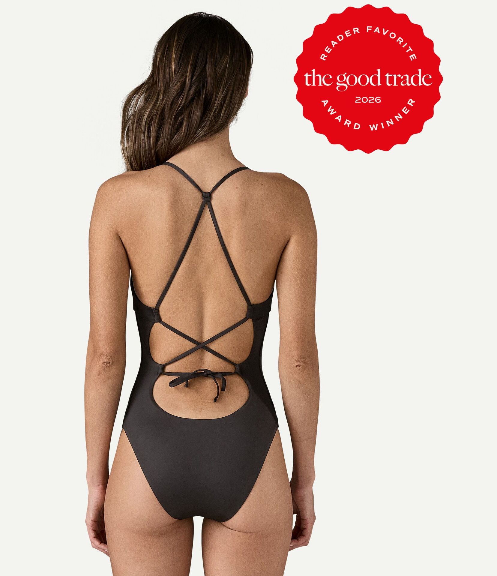 A woman models a black one-piece swimsuit with crisscross straps and an open back. A red badge reads, "The Good Trade 2026 Reader Favorite Award Winner.